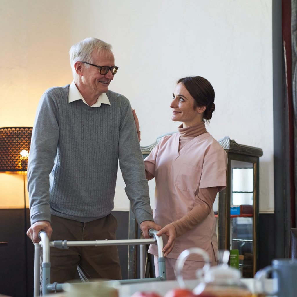 Portrait of smiling young woman helping senior man using walker in nursing home, copy space
